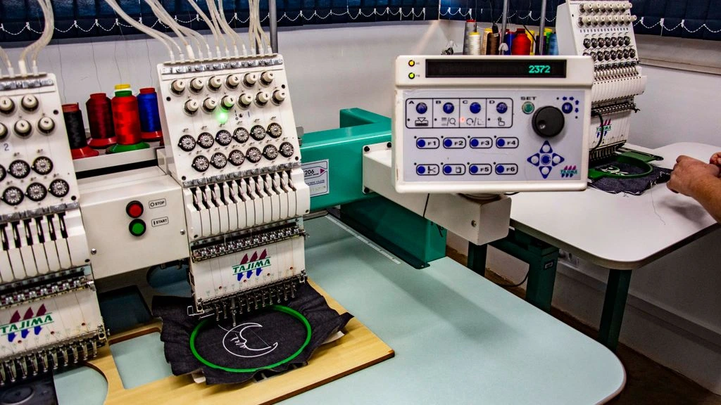 Industrial embroidery machine stitching a logo onto a cream garment